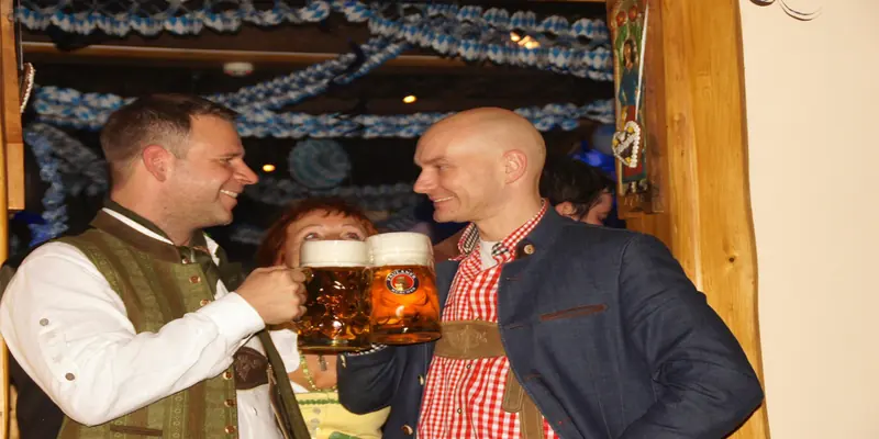 Zwei Gäste in Tracht stoßen mit Maßkrügen an