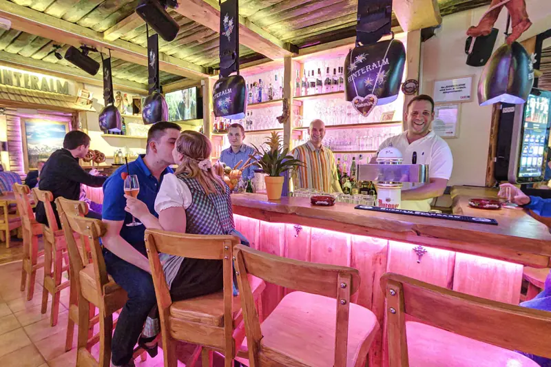 Die Bar der Hinteralm mit rosa beleuchteter Holztheke, Kuhglocken und Gästen